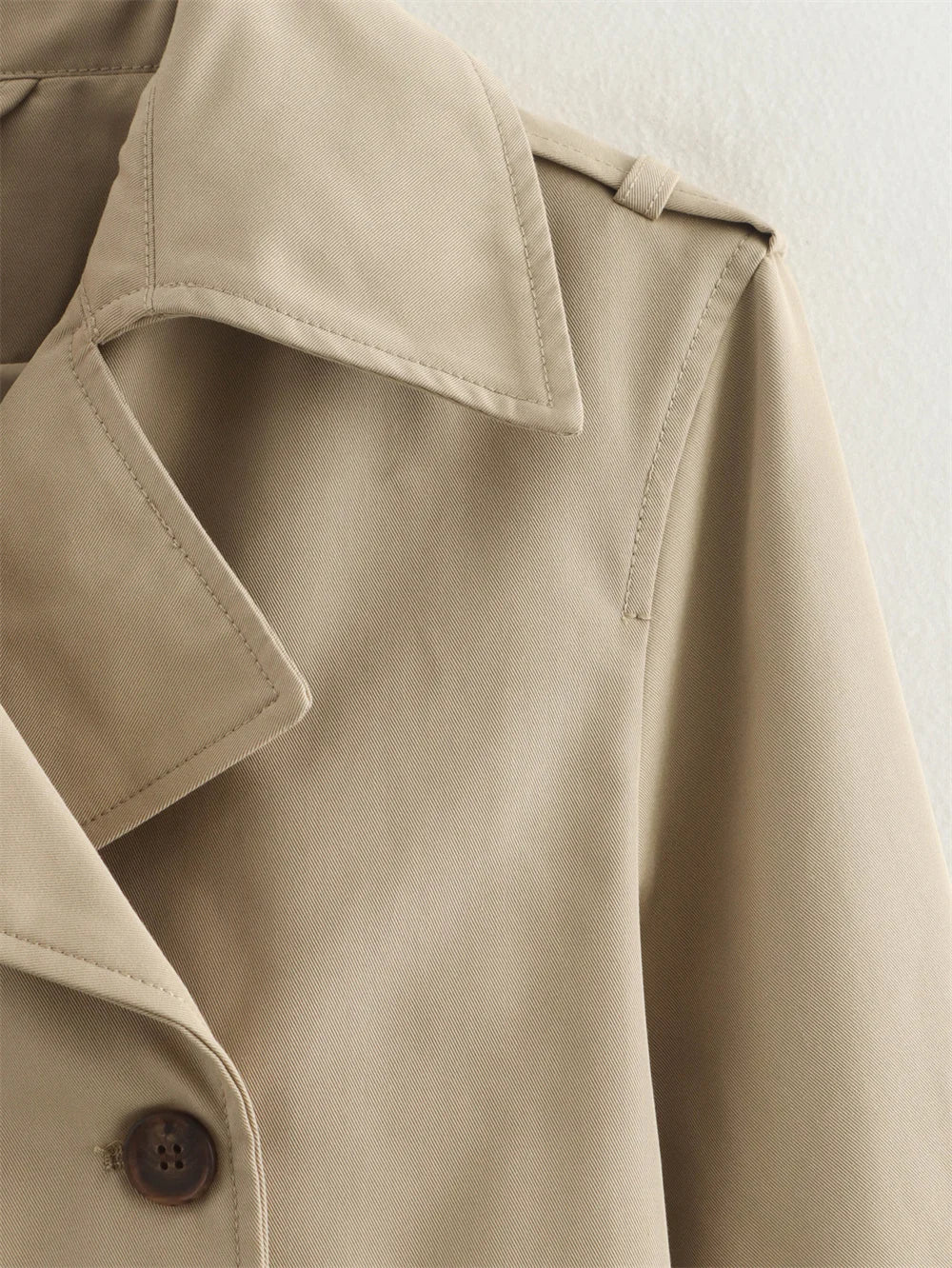 Close-up of a beige trench coat with a button on a light background