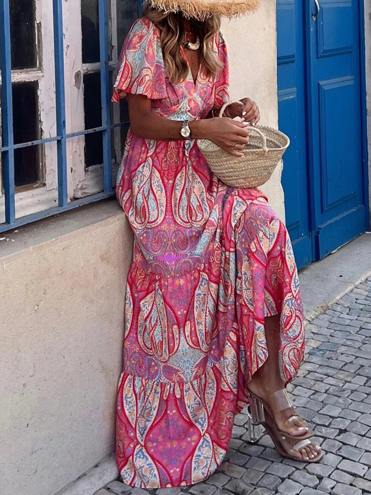 Woman in a long pink patterned dress standing in front of a blue door.