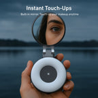 Hand holding a compact mirror with a built-in light, reflecting a person's eye against a blurred natural background.