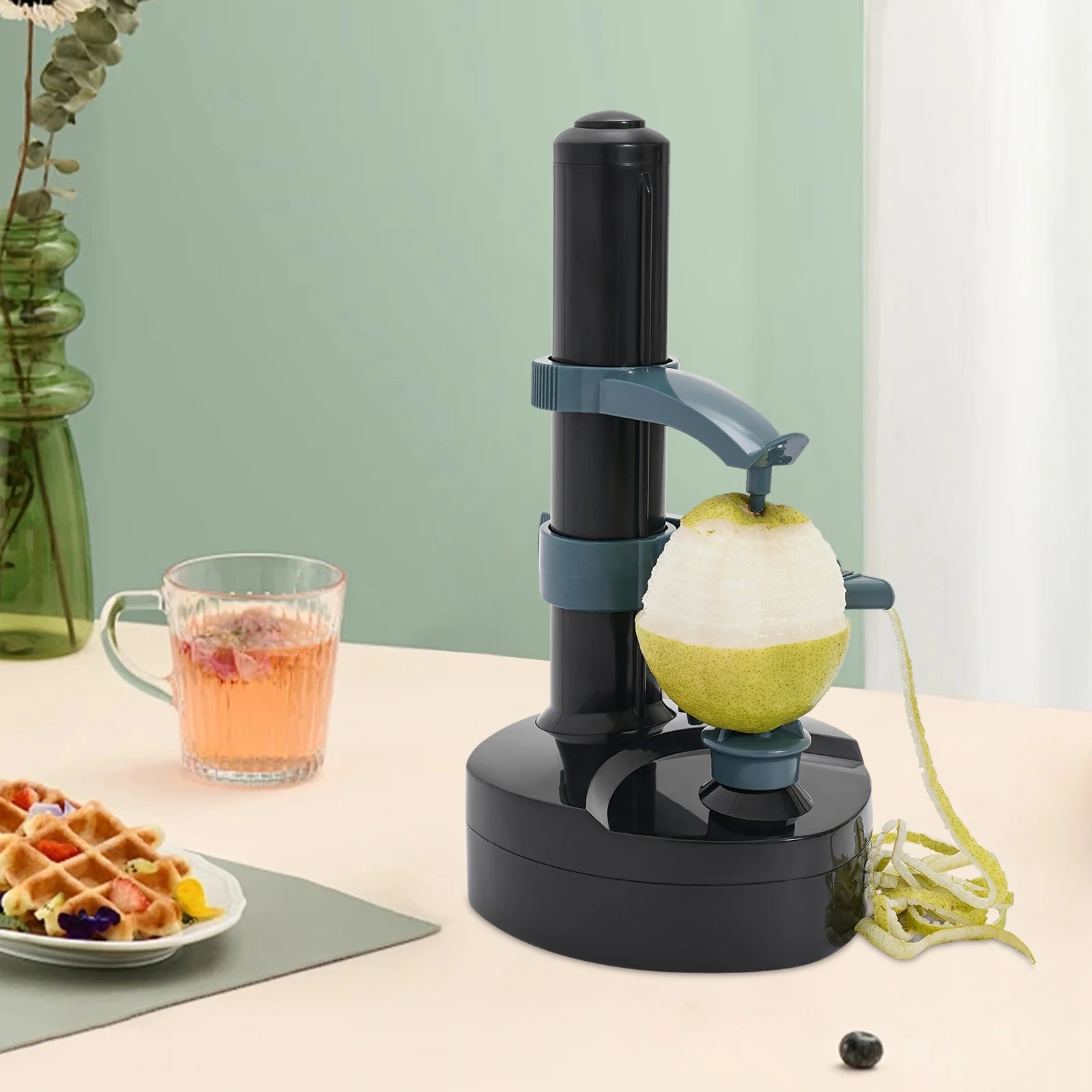 Black apple peeler on a table with a plate of waffles and a glass of juice.
