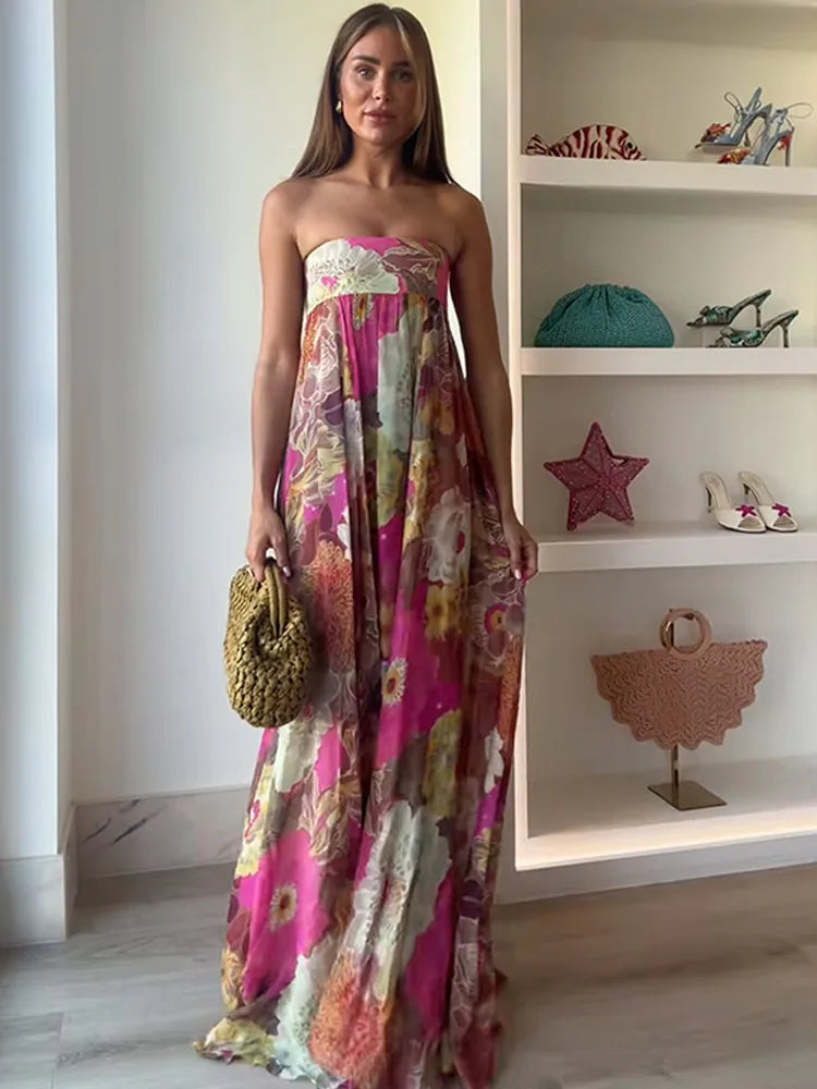 Woman in a colorful strapless dress holding a textured handbag in a room with shelves displaying various items.