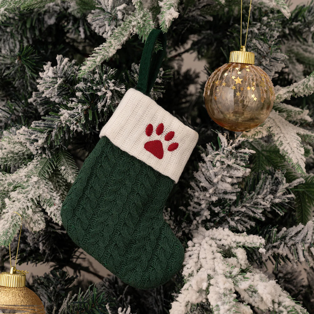 Green and white Christmas stocking with red paw prints on a decorated tree.