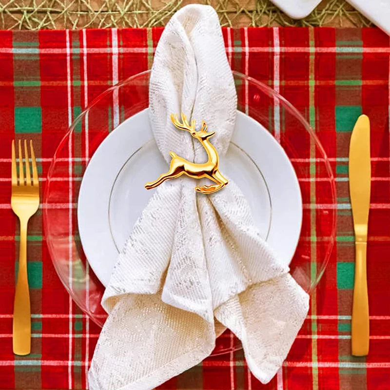Napkin folded with a gold reindeer clip on a white plate against a red plaid tablecloth.