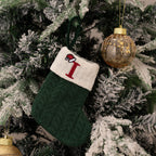 Green knitted stocking with a red letter 'I' hanging on a Christmas tree.