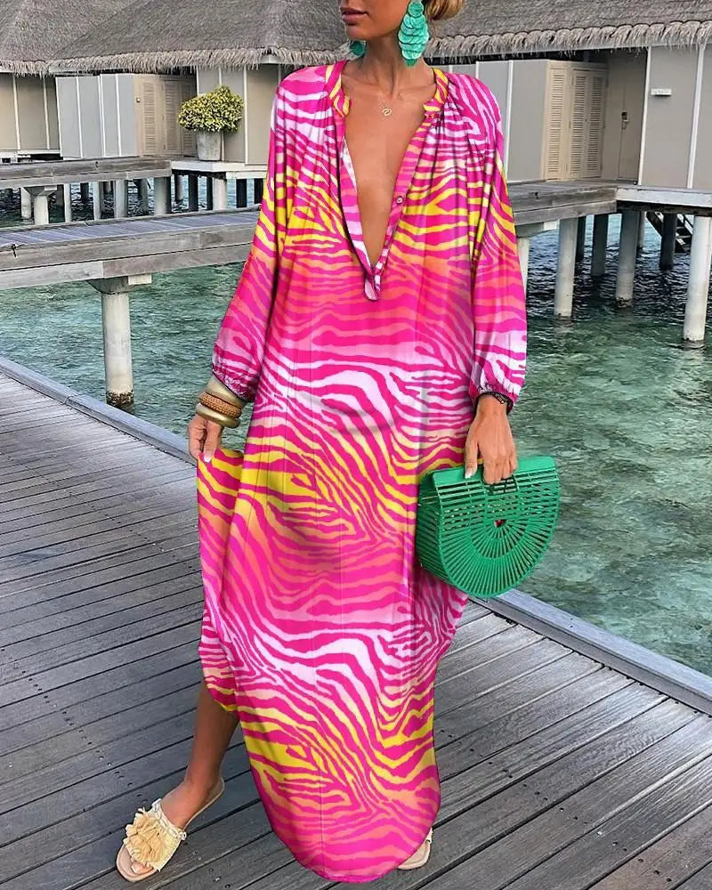 Woman in a vibrant pink and yellow dress standing on a wooden deck by a pool.