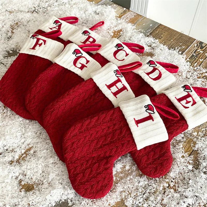 Red and white Christmas stockings with lettering on a wooden surface.