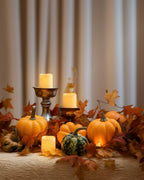 Autumnal centerpiece with pumpkins, candles, and leaves on a wooden surface.