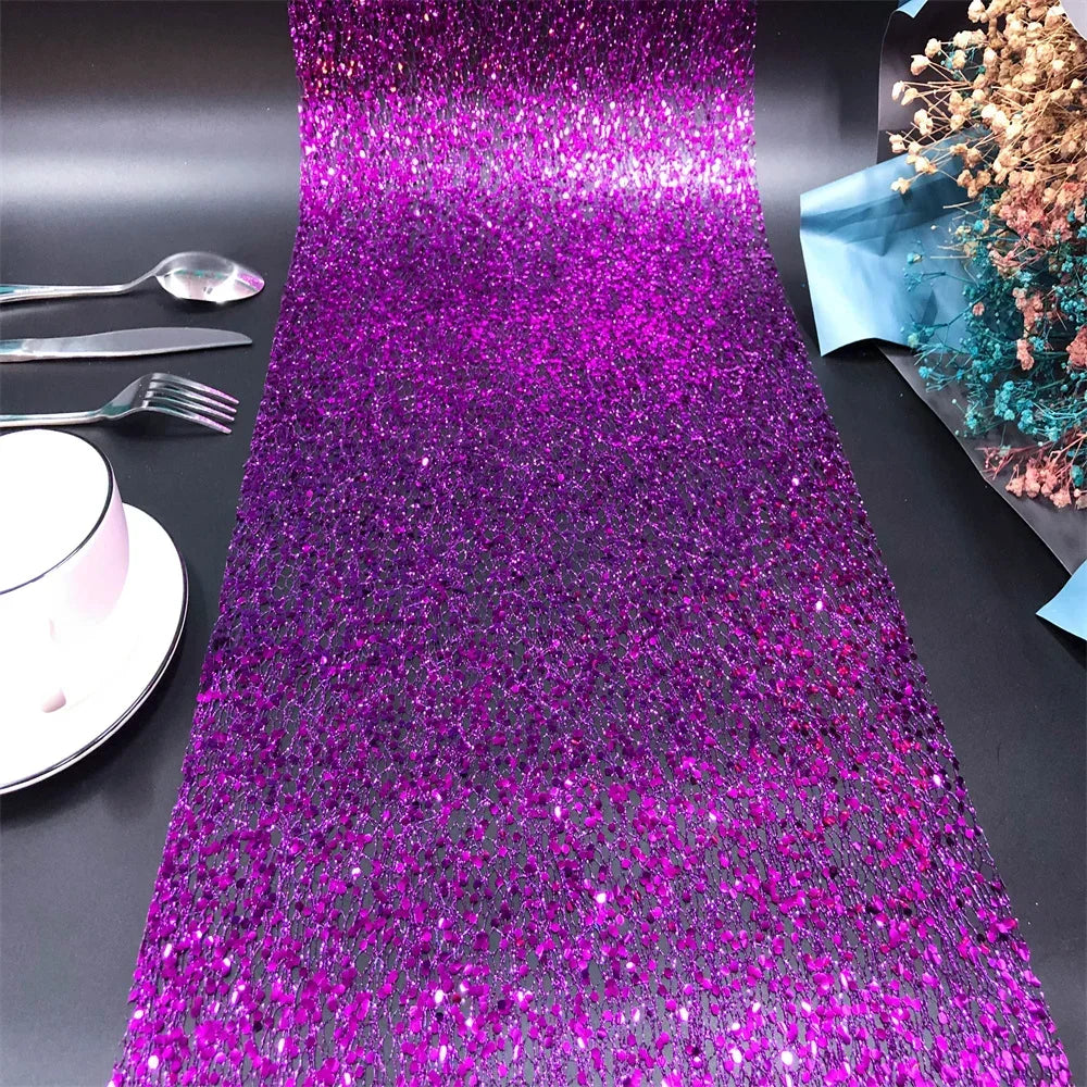 Purple glittery table runner on a black surface with silverware and a cup.