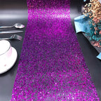 Purple glittery table runner on a black surface with silverware and a cup.