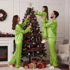 Family in matching green outfits decorating a Christmas tree in a living room.