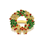 Gold wreath-shaped ring with green leaves, red berries, and clear stones on a white background