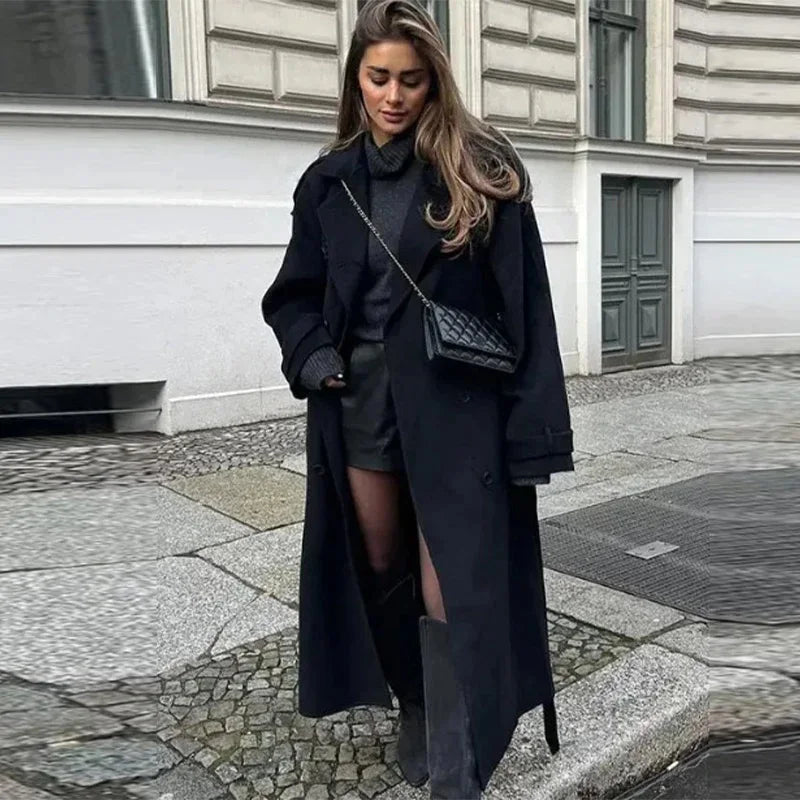 Woman in a black coat and outfit standing on a street.