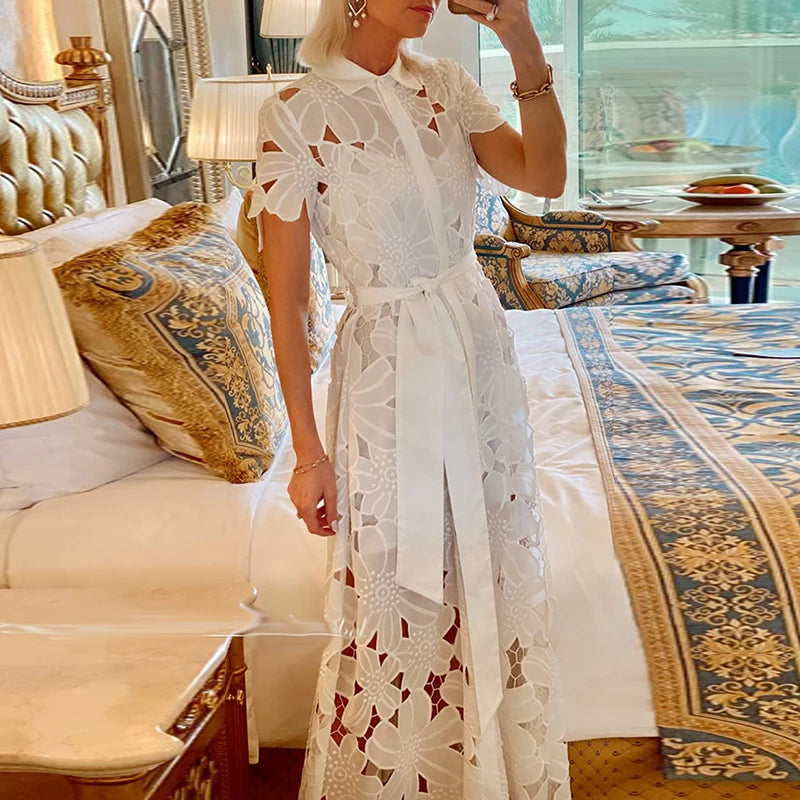 Woman in a white lace dress standing in an elegant room with decorative furniture.