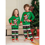 Two children wearing matching green Christmas pajamas with Santa Claus designs in a living room.