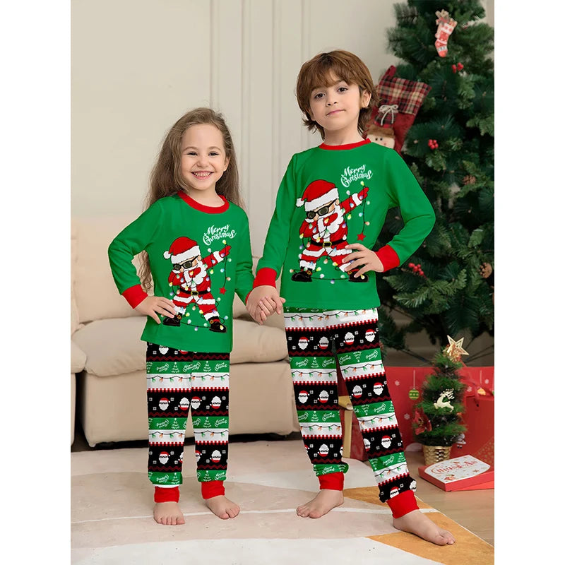 Two children wearing matching green Christmas pajamas with Santa Claus designs in a living room.