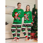 Two people wearing matching green Christmas pajamas with Santa Claus designs in a living room.
