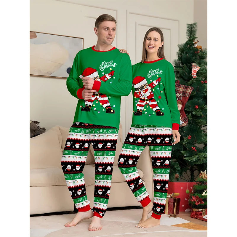 Two people wearing matching green Christmas pajamas with Santa Claus designs in a living room.