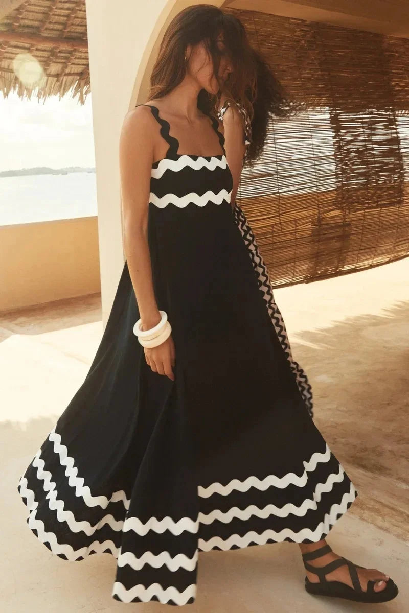 Woman wearing a black and white dress with a wavy pattern, standing in a sunlit room.