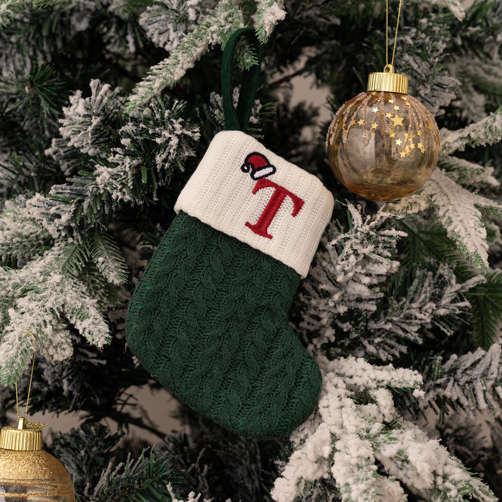 Green and white Christmas stocking with a red letter 'T' on a decorated tree.
