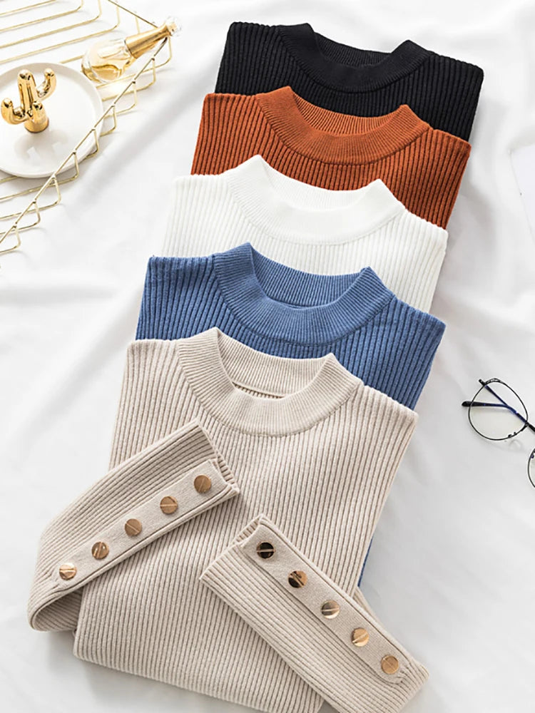 Five folded sweaters in black, brown, white, blue, and beige on a light surface.