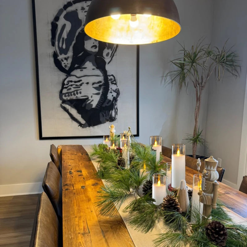 Dining room with a long wooden table set for a meal, featuring candles and greenery.