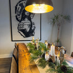 Dining room with a long wooden table set for a meal, featuring candles and greenery.