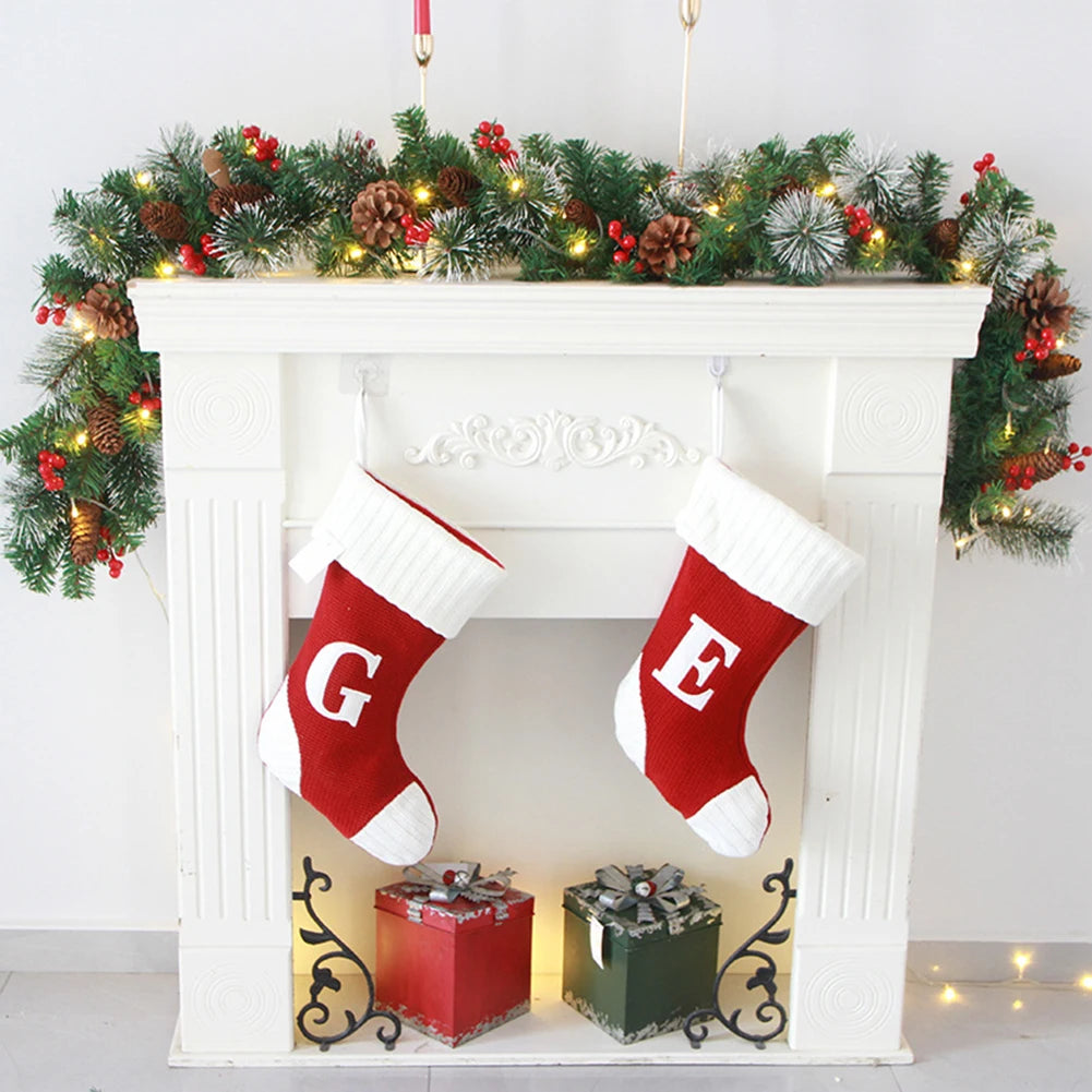 Two red Christmas stockings with white trim hanging on a fireplace mantle decorated with a garland and lights.