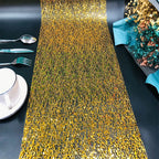 Gold sequin table runner on a black table with silverware and a cup.