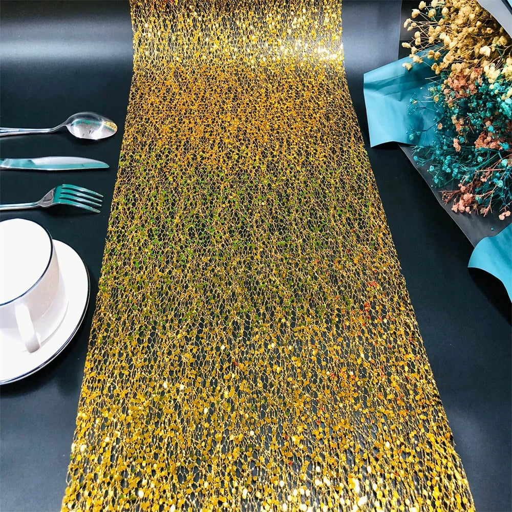 Gold sequin table runner on a black table with silverware and a cup.
