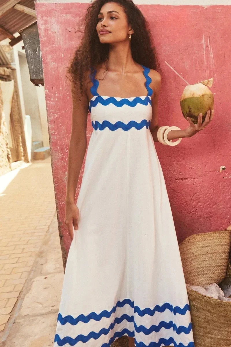 Woman in a white dress with blue accents holding a coconut against a pink wall.