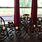 Decorative black metal candle holders with candles on a table in front of red curtains.