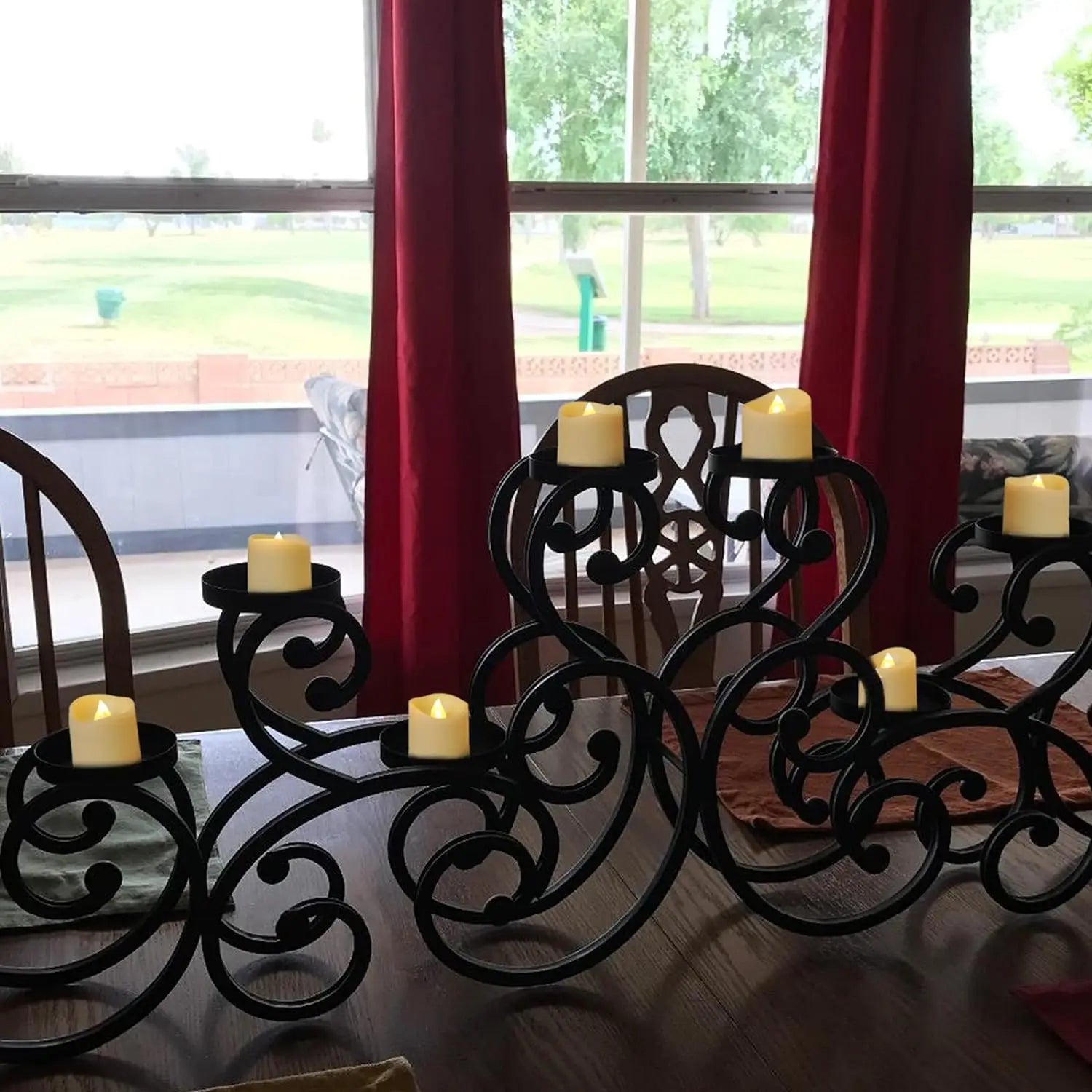 Decorative black metal candle holders with candles on a table in front of red curtains.