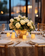 Decorative table setting with white roses, candles, and cutlery in a warm indoor setting.