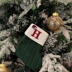 Green knitted stocking with a red 'H' ornament on a decorated Christmas tree.