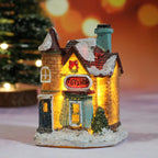 Decorative toy shop house with glowing interior, snow on roof, and Christmas tree in the background.