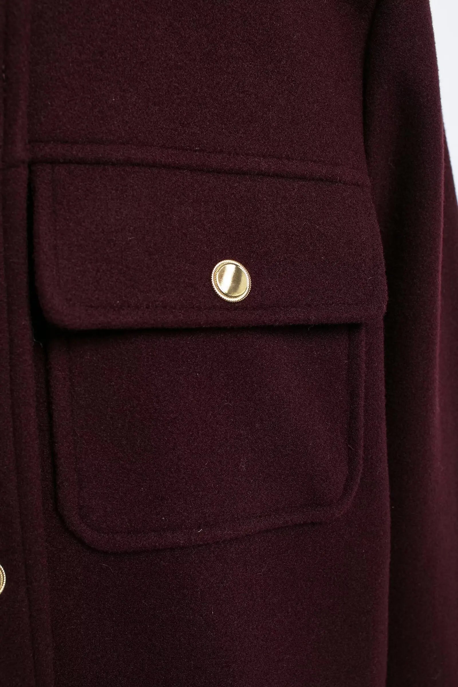 Close-up of a burgundy coat with a gold button on a white background