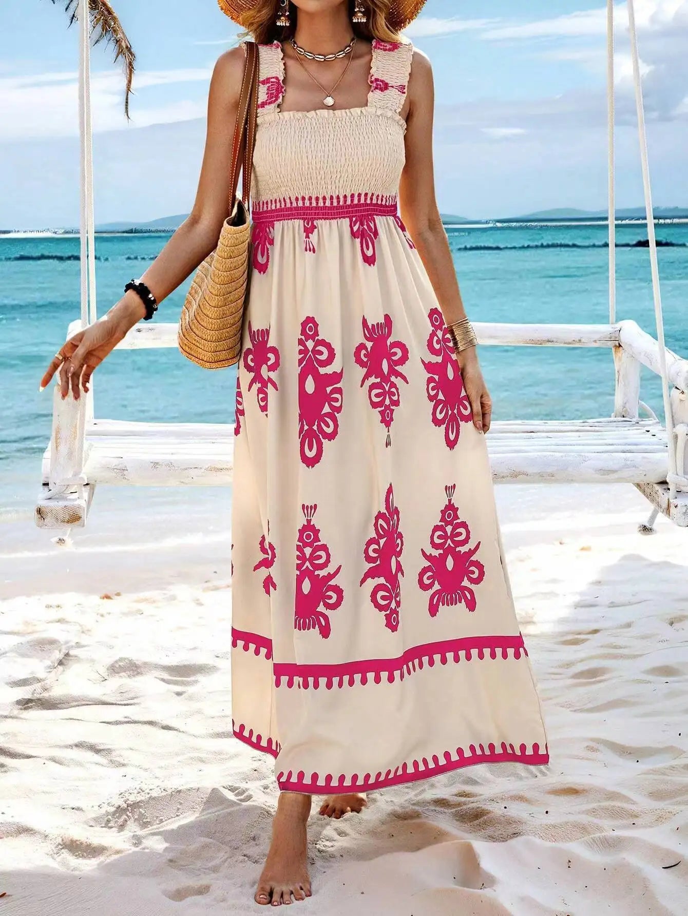 Woman in a beige dress with pink patterns standing on a sandy beach.