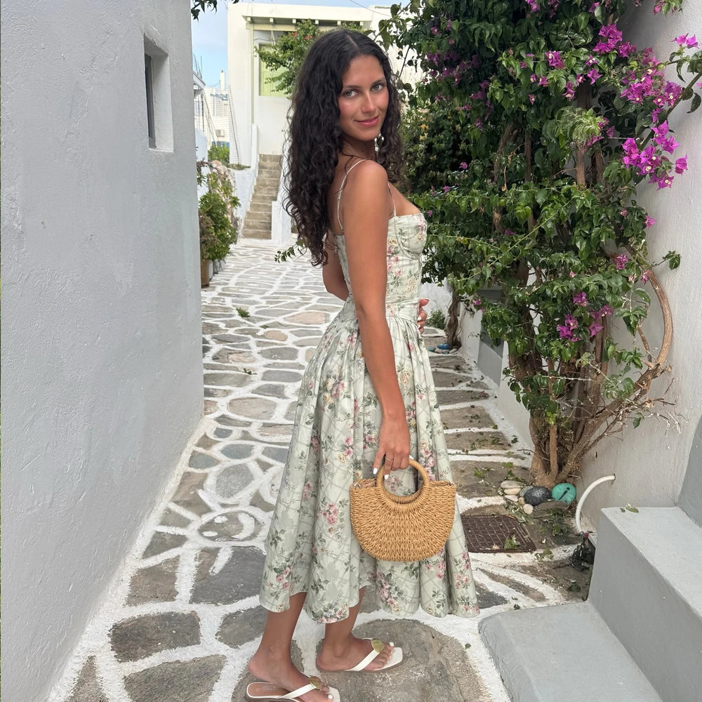 Woman in a floral dress standing on a picturesque street with white buildings and greenery.