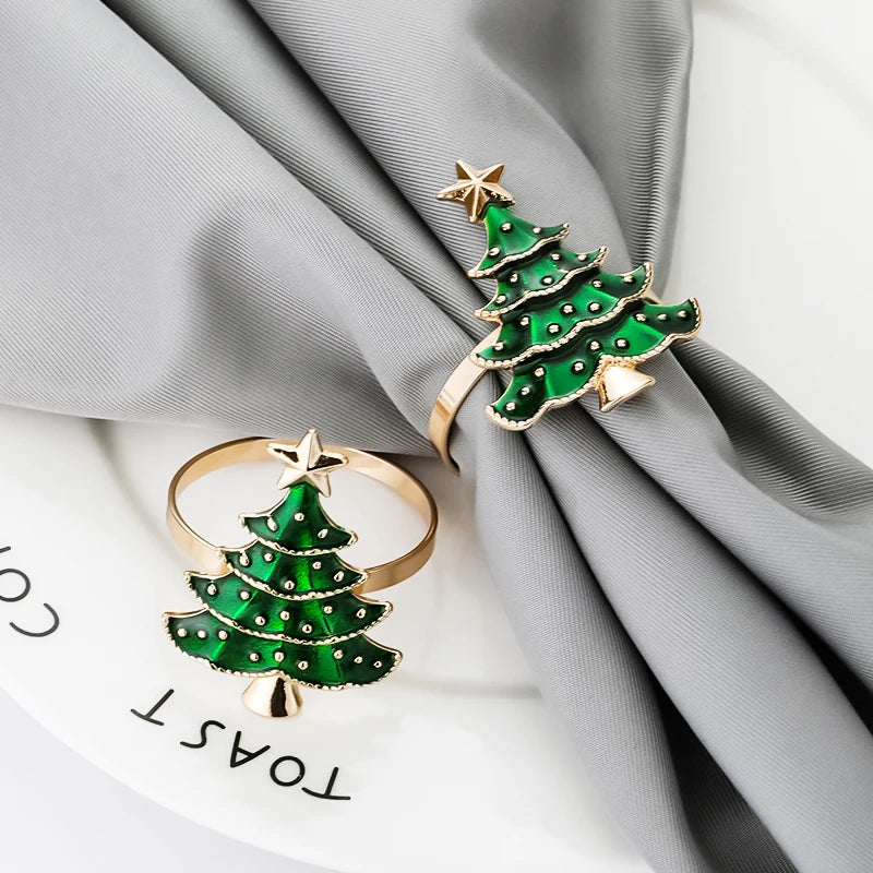 Two green Christmas tree-shaped rings with gold accents on a gray fabric background.