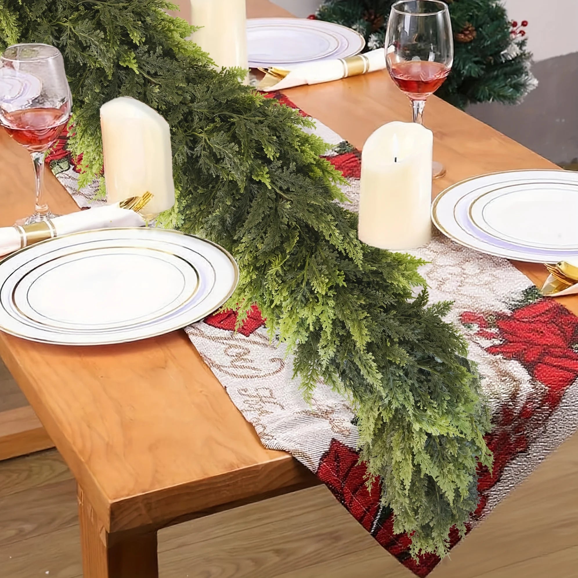 Dining table set for Christmas with greenery, candles, and red and white tablecloth.