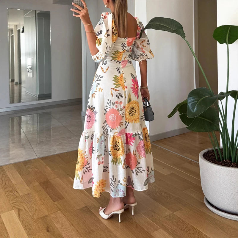 Woman in a floral dress taking a mirror selfie in a room with a plant.