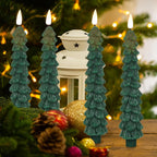 Four teal Christmas tree-shaped candles with a white lantern and ornaments on a wooden surface.