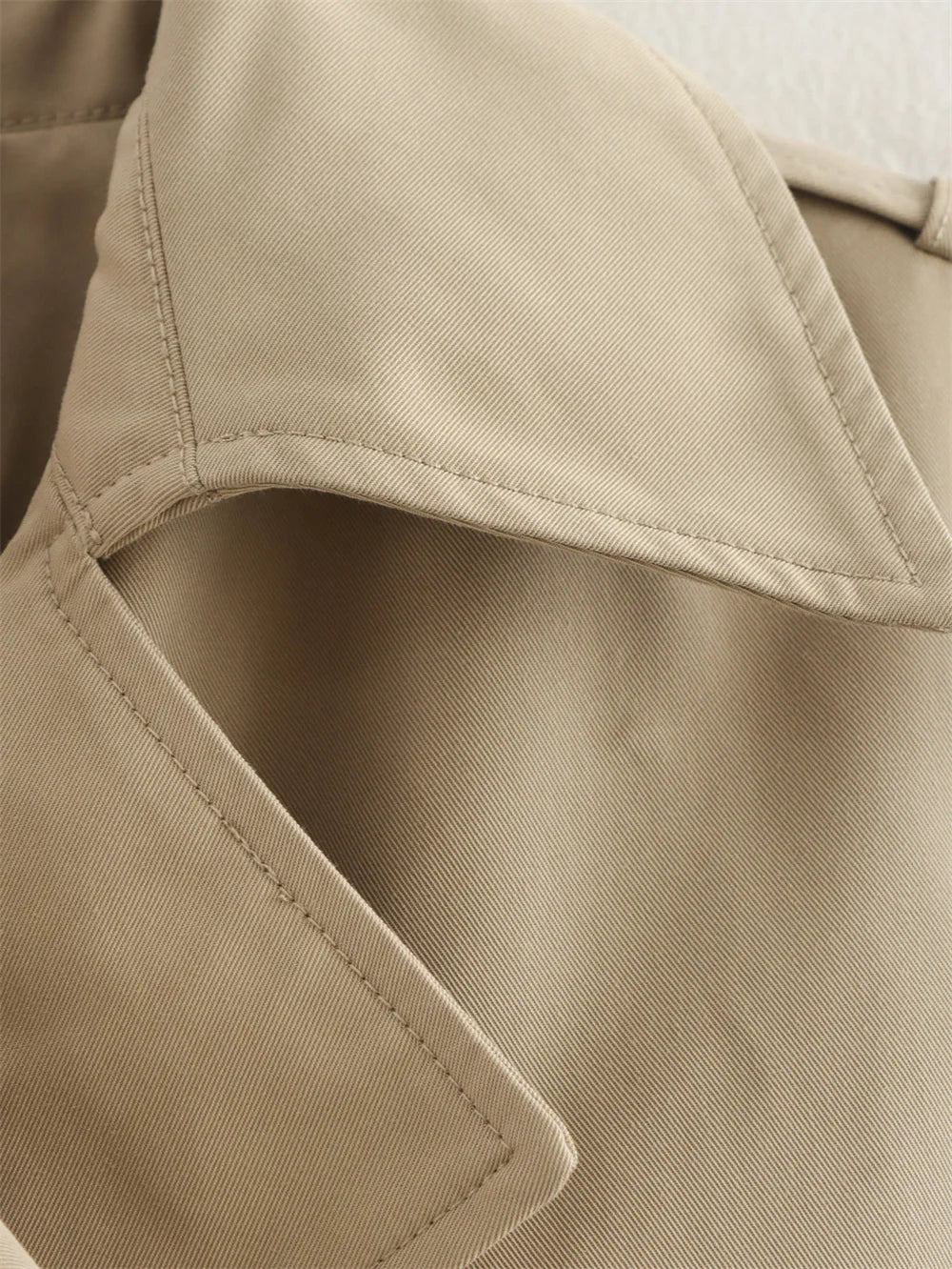 Close-up of a beige trench coat with a focus on texture and stitching.
