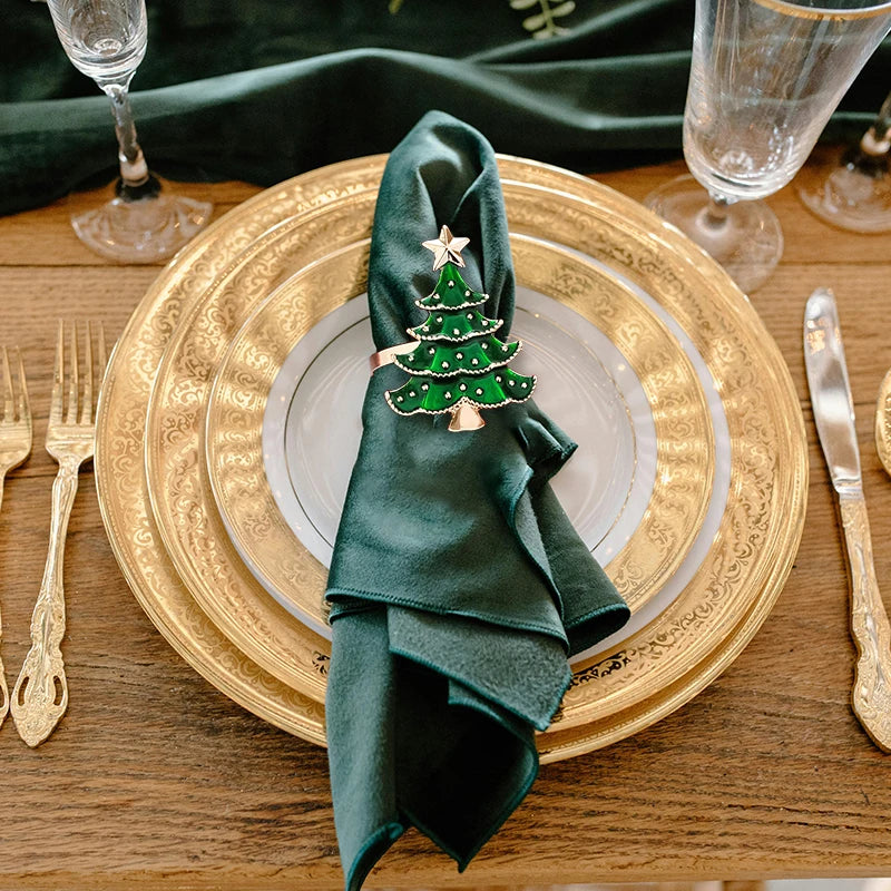 Green napkin with a Christmas tree ornament on a gold charger plate with cutlery and glasses.