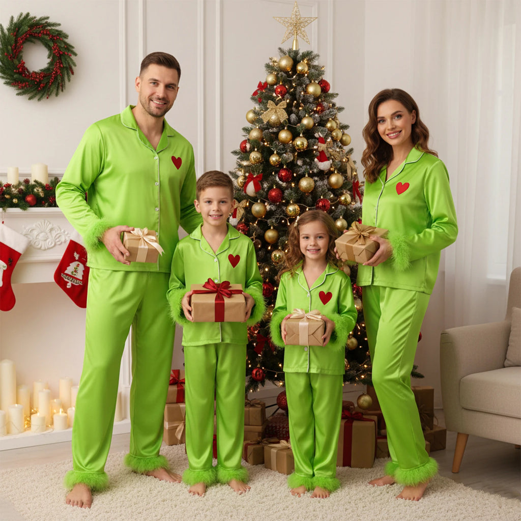 Family in matching green pajamas holding Christmas presents in front of a decorated tree.