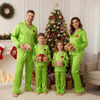 Family in matching green pajamas holding Christmas presents in front of a decorated tree.