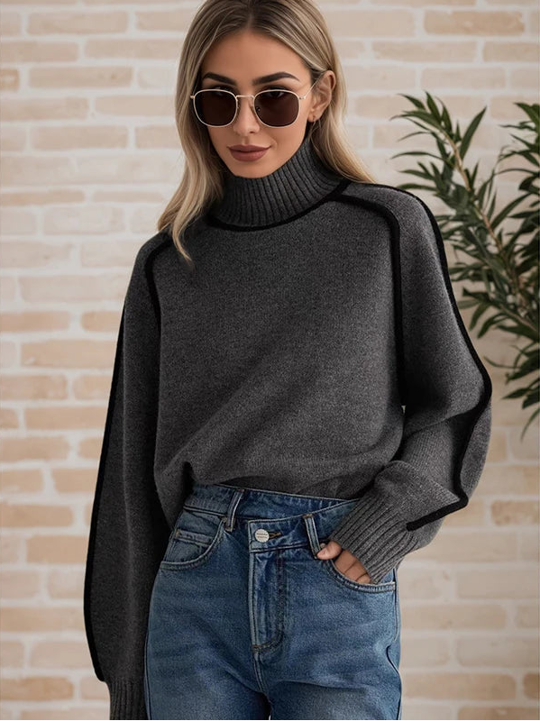 Woman wearing a dark gray turtleneck sweater and blue jeans against a brick wall.
