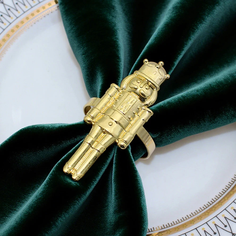 Gold astronaut-shaped napkin ring on a green velvet fabric with a white and gold decorative background.