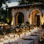 Elegant outdoor dinner table setting with candles and flowers in front of a stone building.