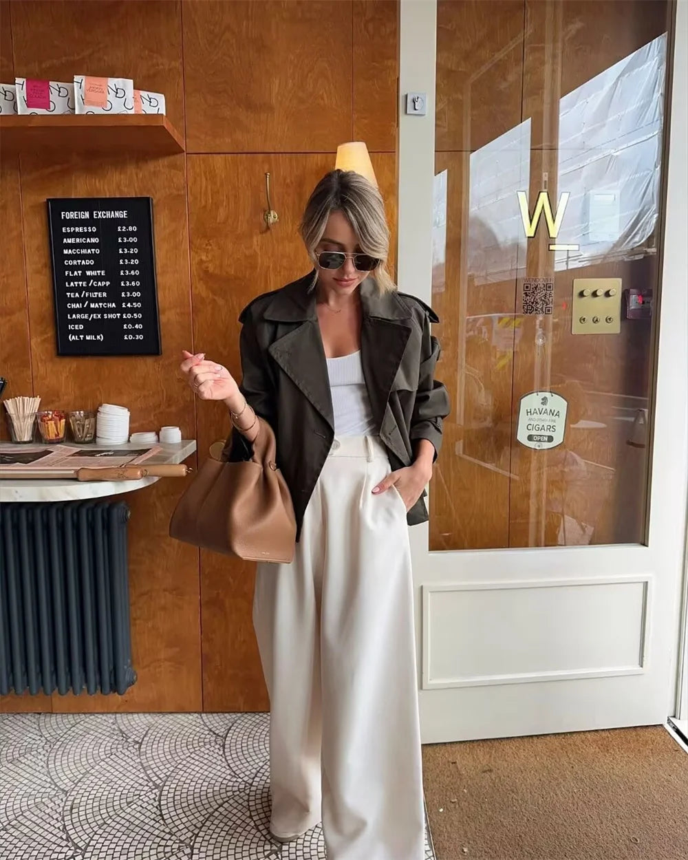 Woman in a stylish outfit standing in front of a wooden door with a glass panel.
